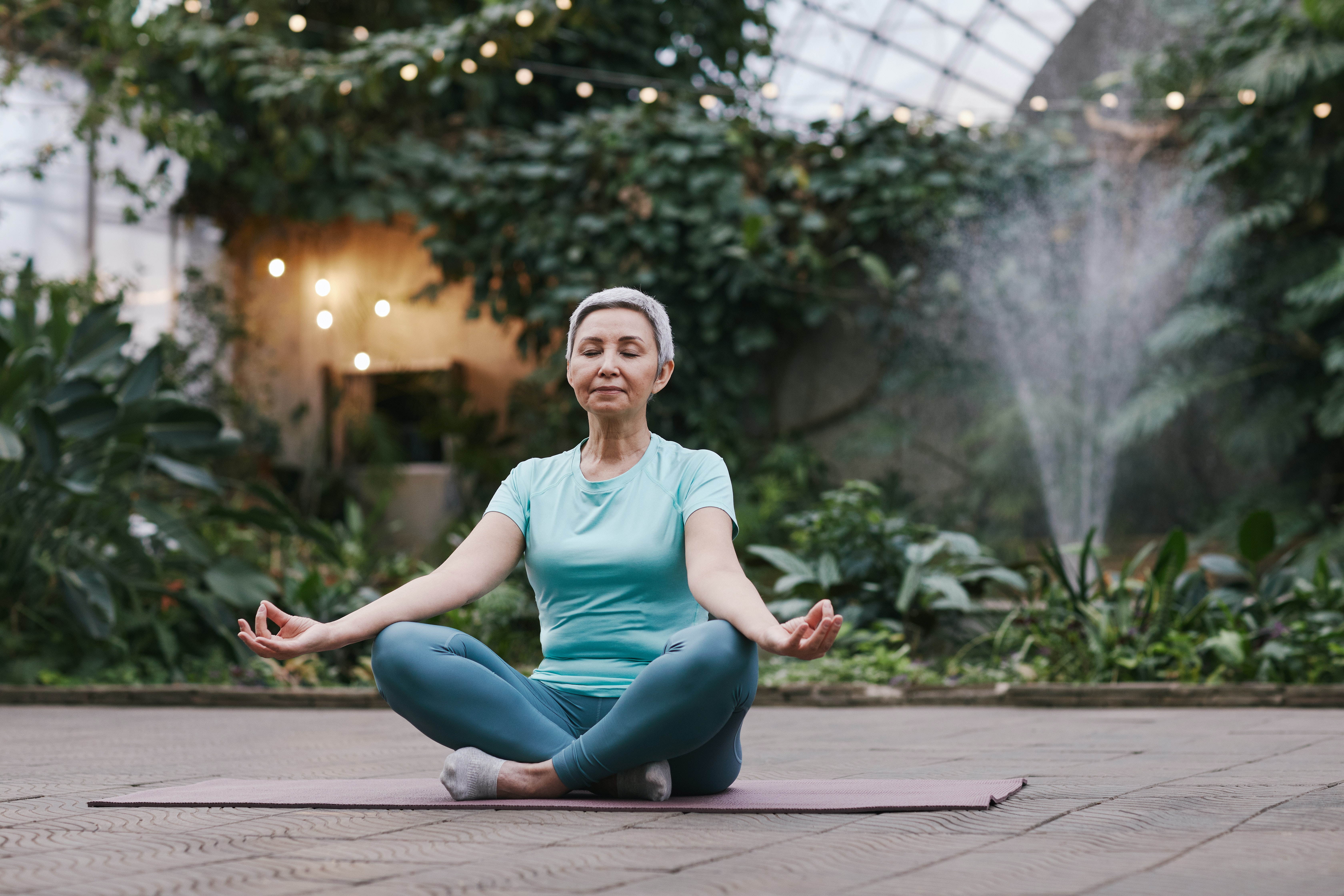 older woman meditating in front of plants